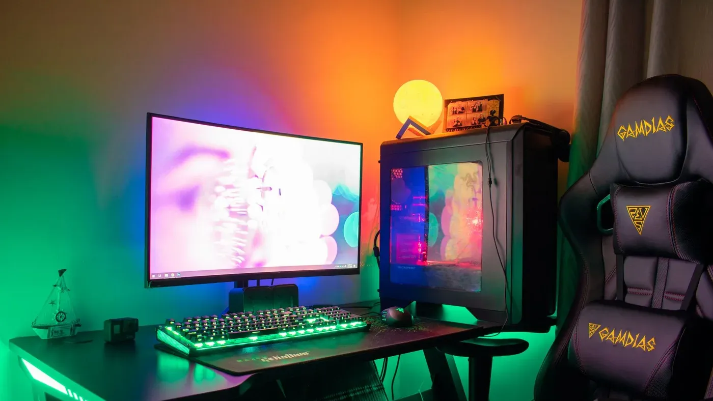 Färgstark gamingsetup med dator, skärm och gamingstol i rgb-belysning i ett mörkt rum
