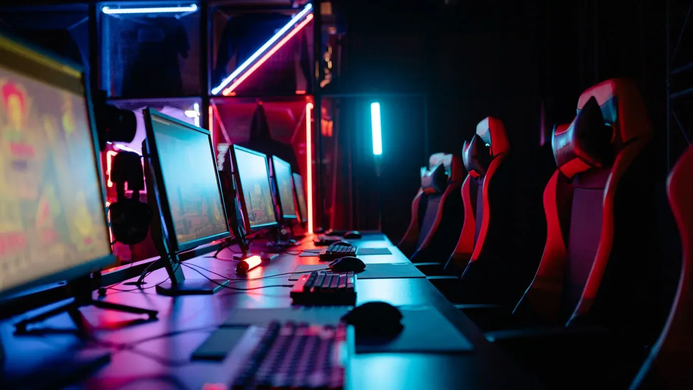 Gamingrum med neonljus, datorer och gamingstolar.