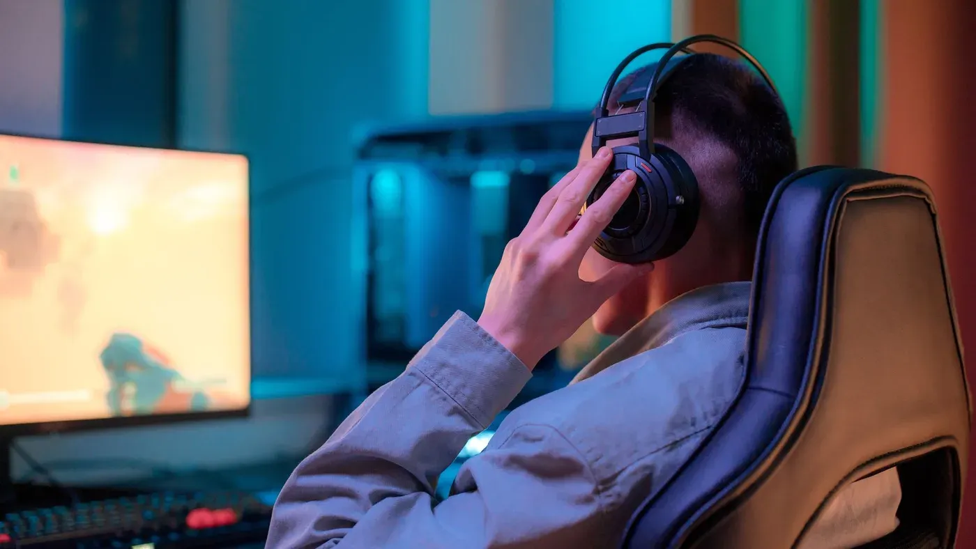 Man med hörlurar spelar dator vid ett snyggt inrett skrivbord.