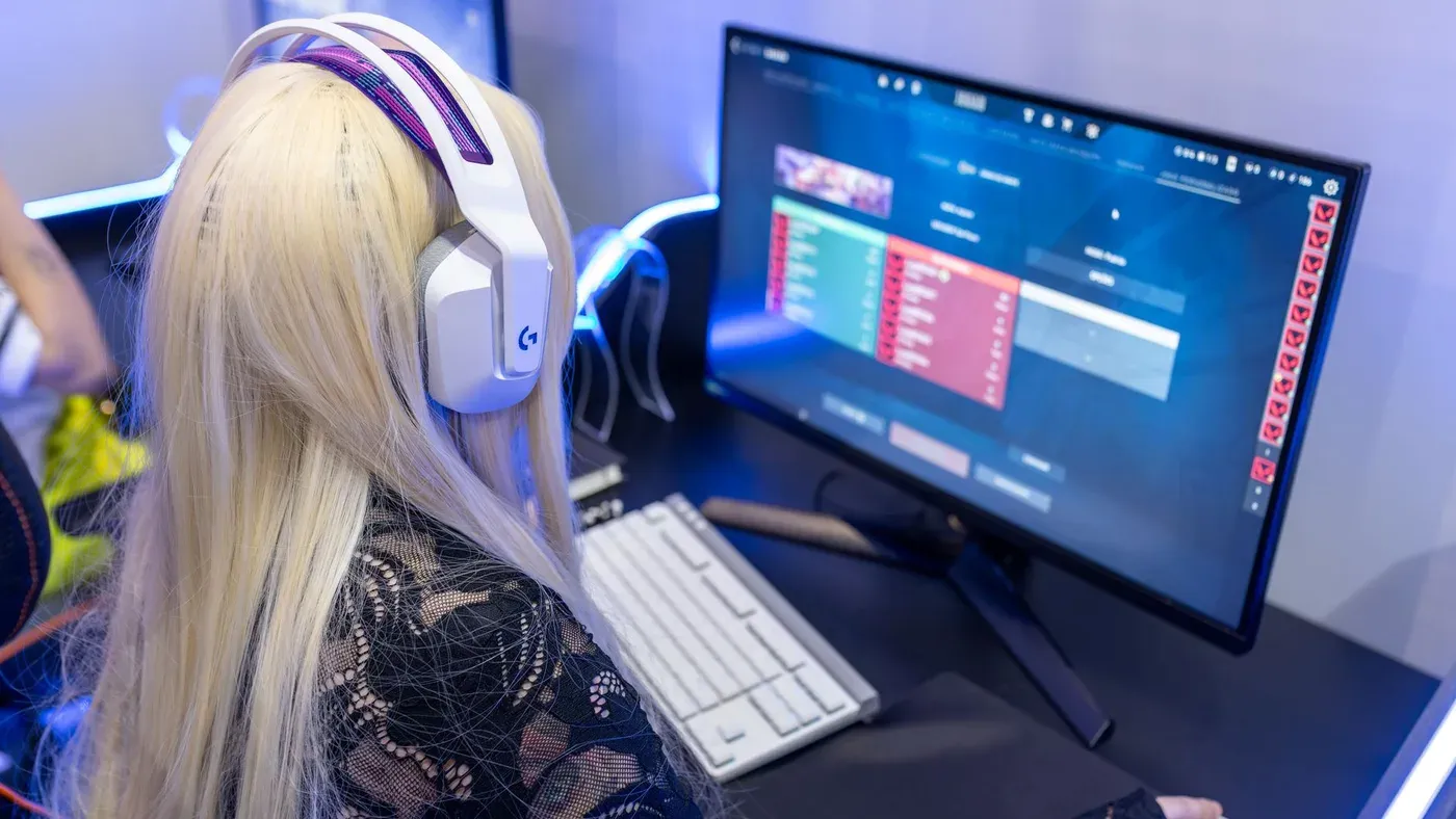Ung kvinna spelar dator med hörlurar på i en modern gamingmiljö.