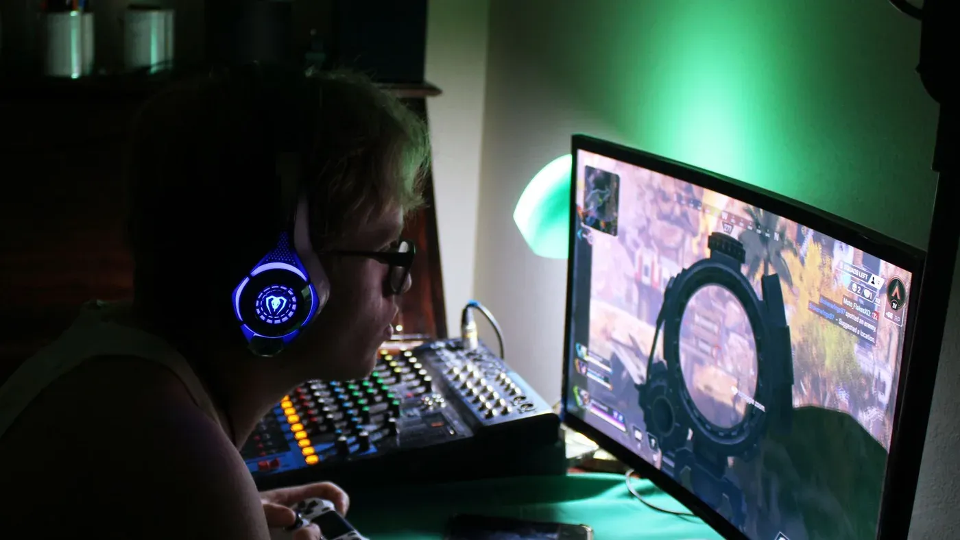Person med headset och handkontroll fördjupad i ett spel, belyst av grönt ljus.