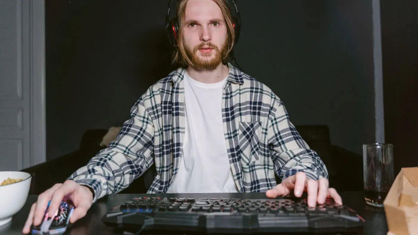 Ung man i rutig skjorta spelar med headset hemma.