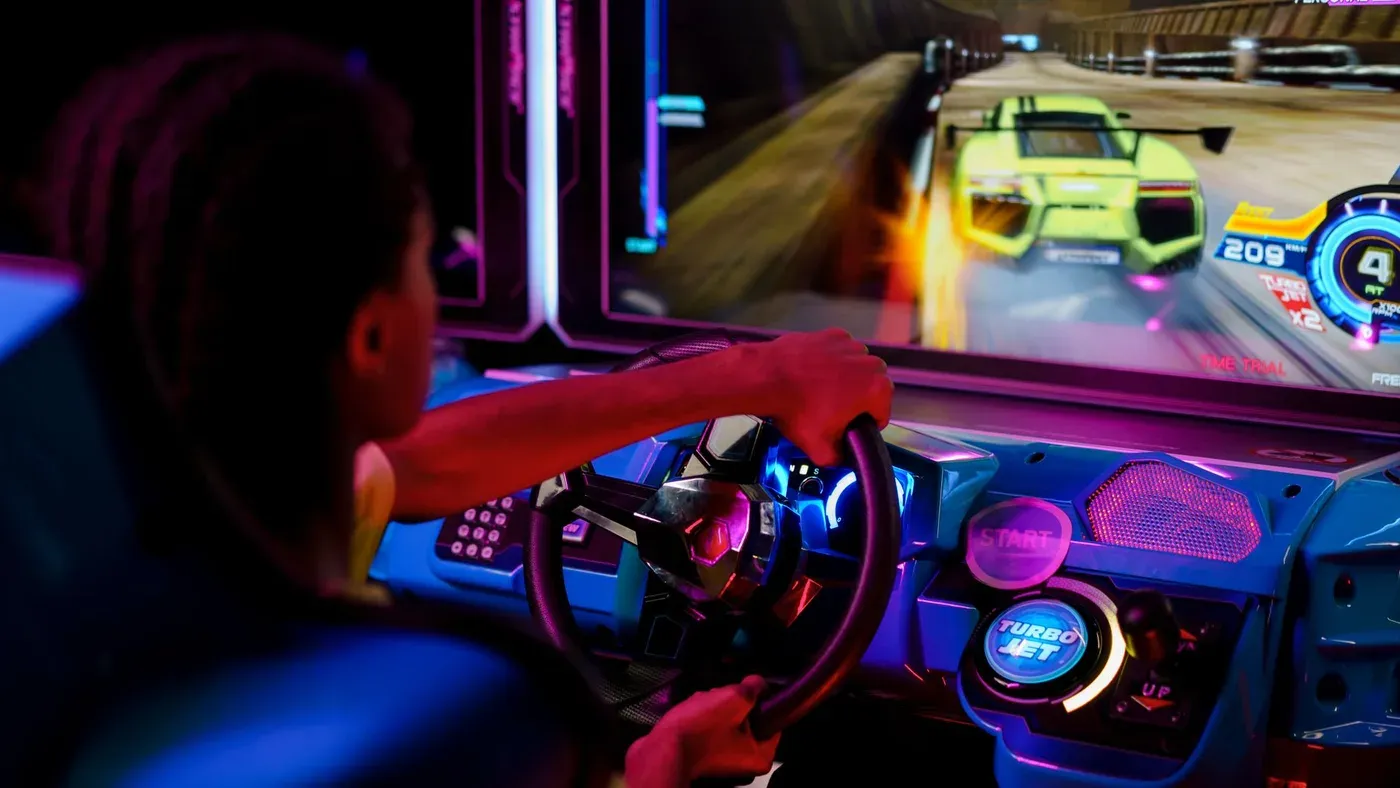 Person spelar ett racingspel i en arkadmiljö med färgstark belysning.