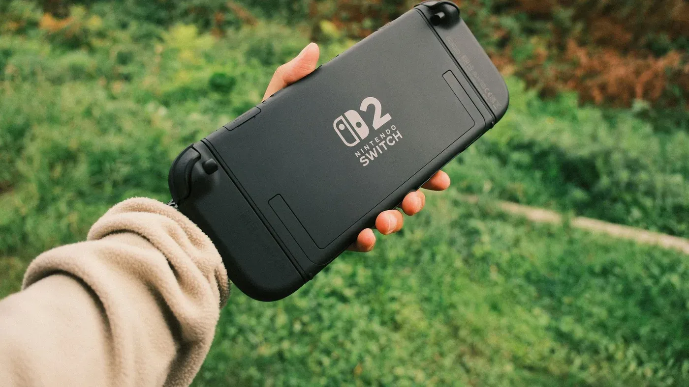 Person håller en Nintendo Switch utomhus i naturmiljö.