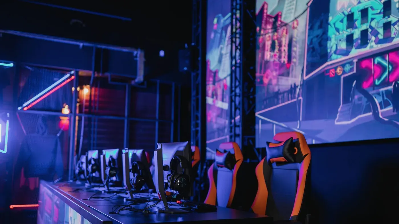 Gamingmiljö med flera skärmar och ergonomiska stolar i neonbelysning.
