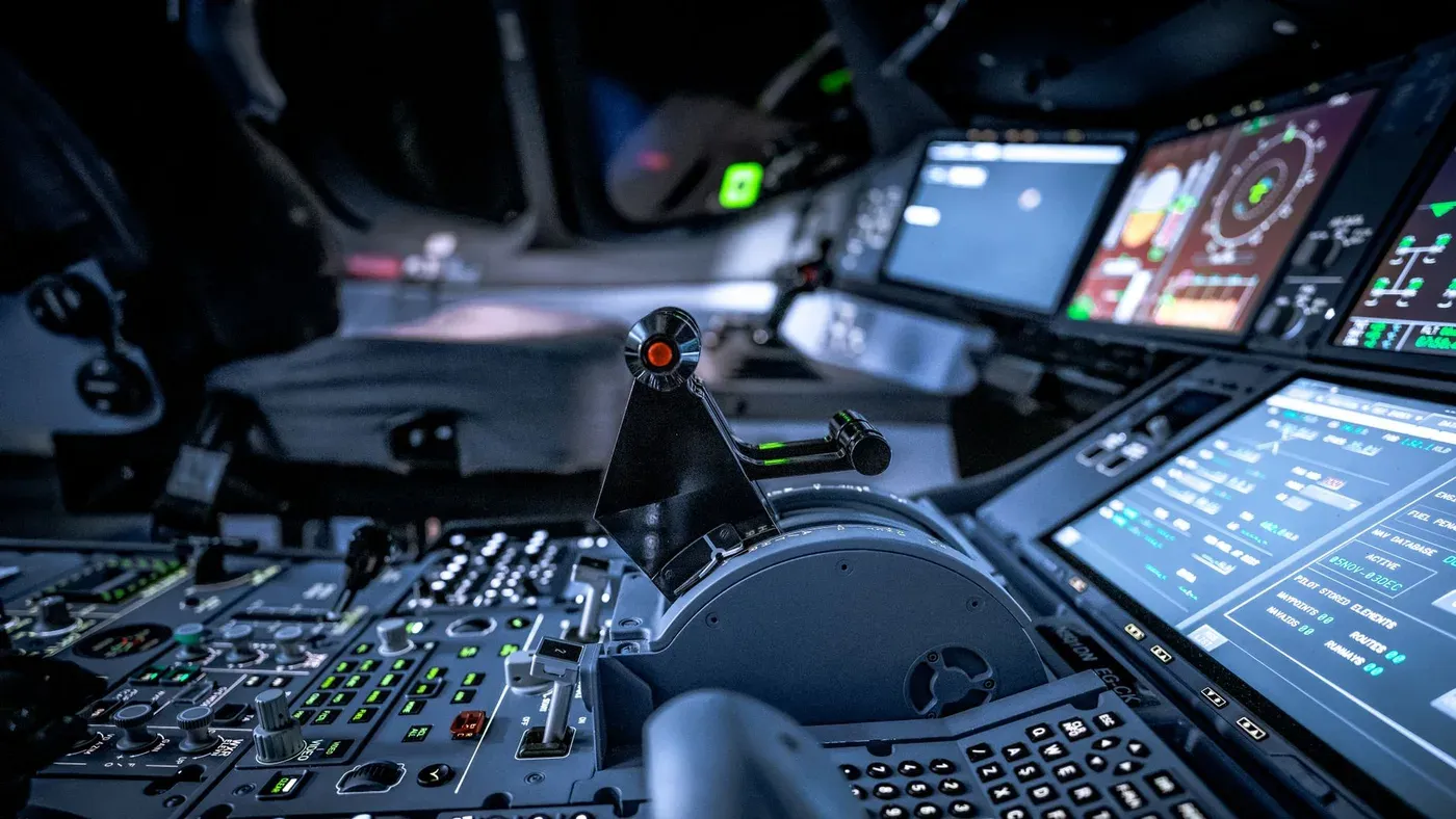 Närbild på en modern flygplanscockpit med upplysta kontrollpaneler och skärmar.