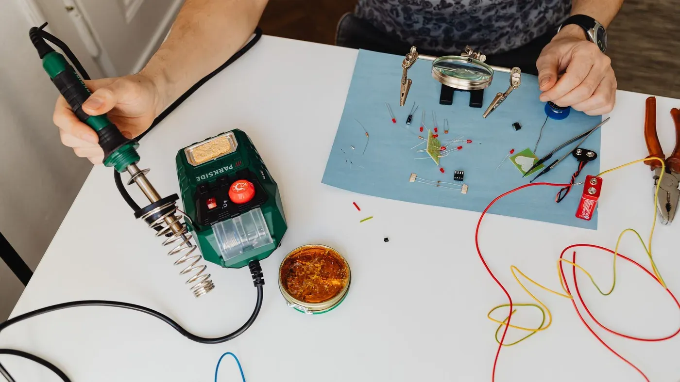 Närbild på händer som löder elektronik med verktyg på en arbetsbänk